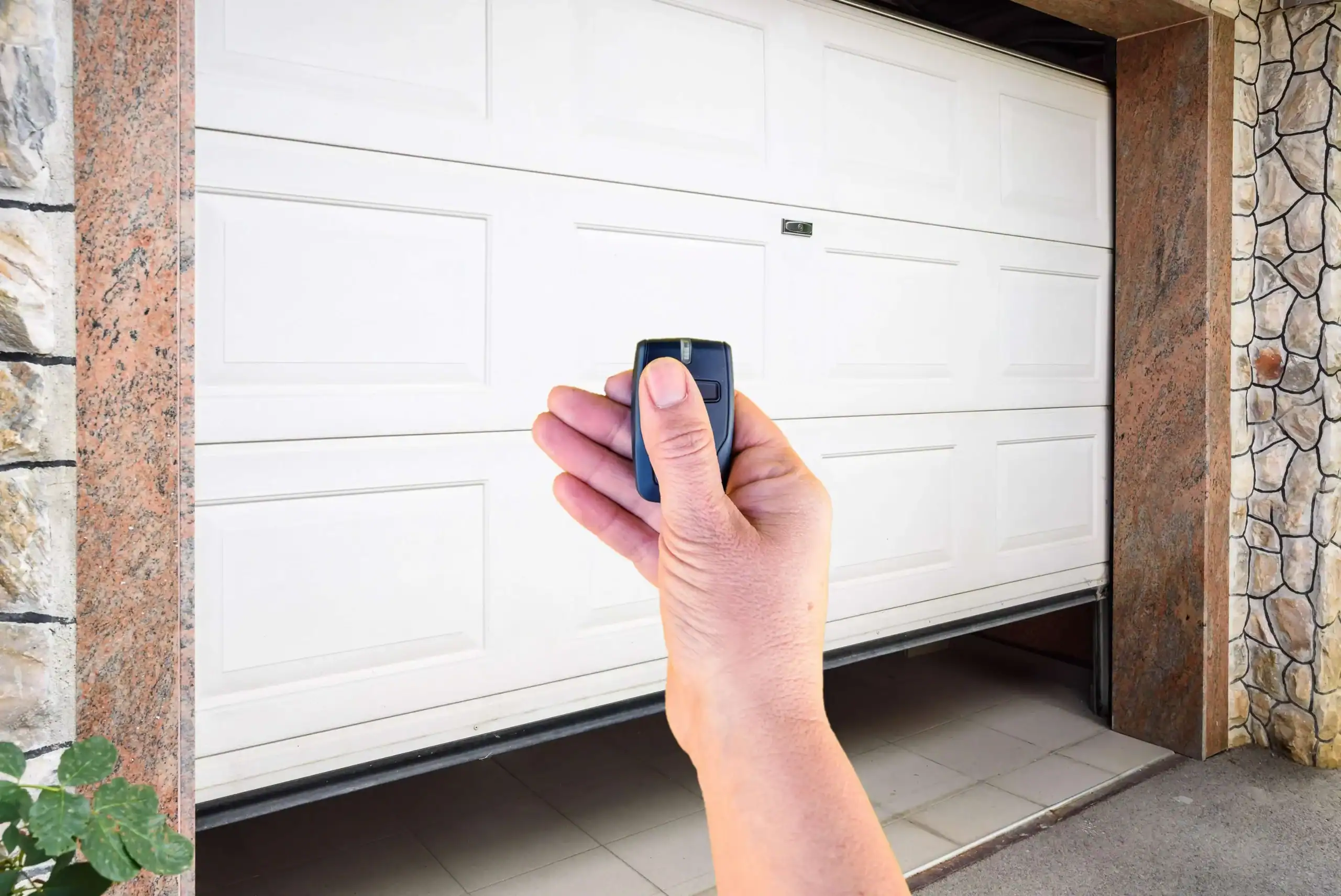 Hand holding a garage door remote in front of a closed garage